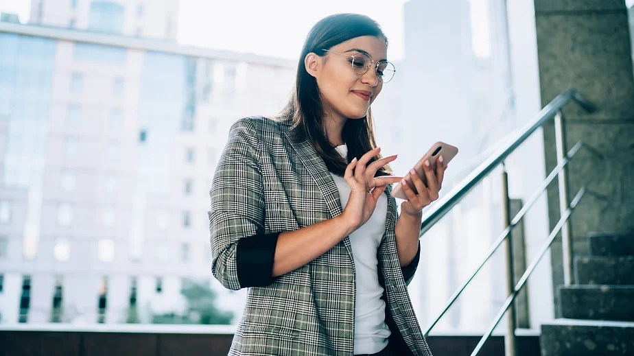woman wearing glasses looking down at mobile phone