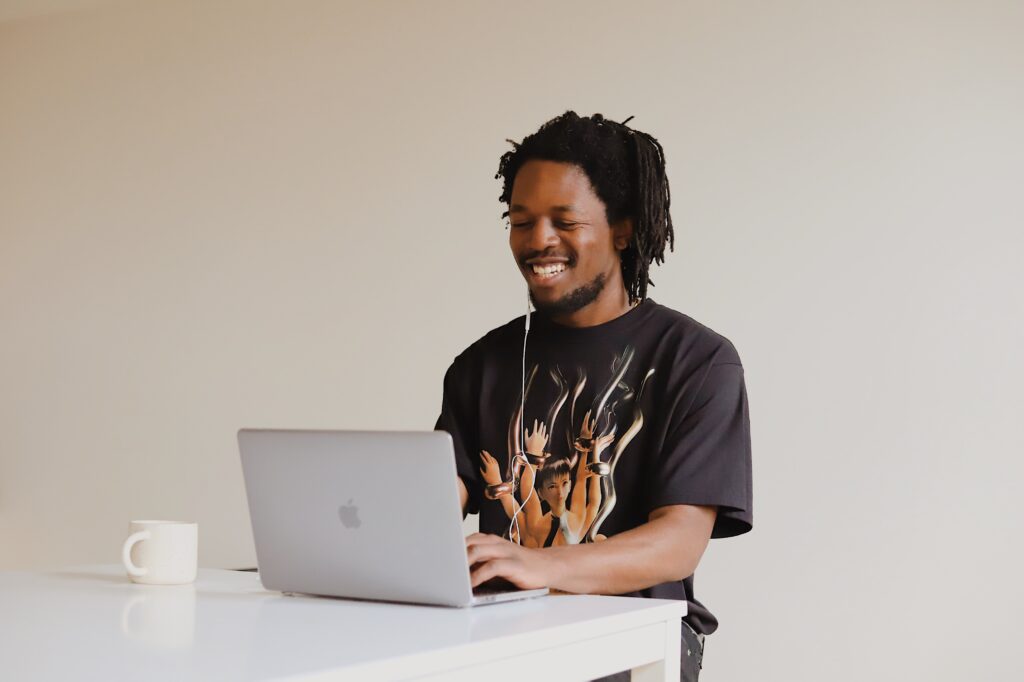 man smiling while looking at laptop screen on desk with coffee mug