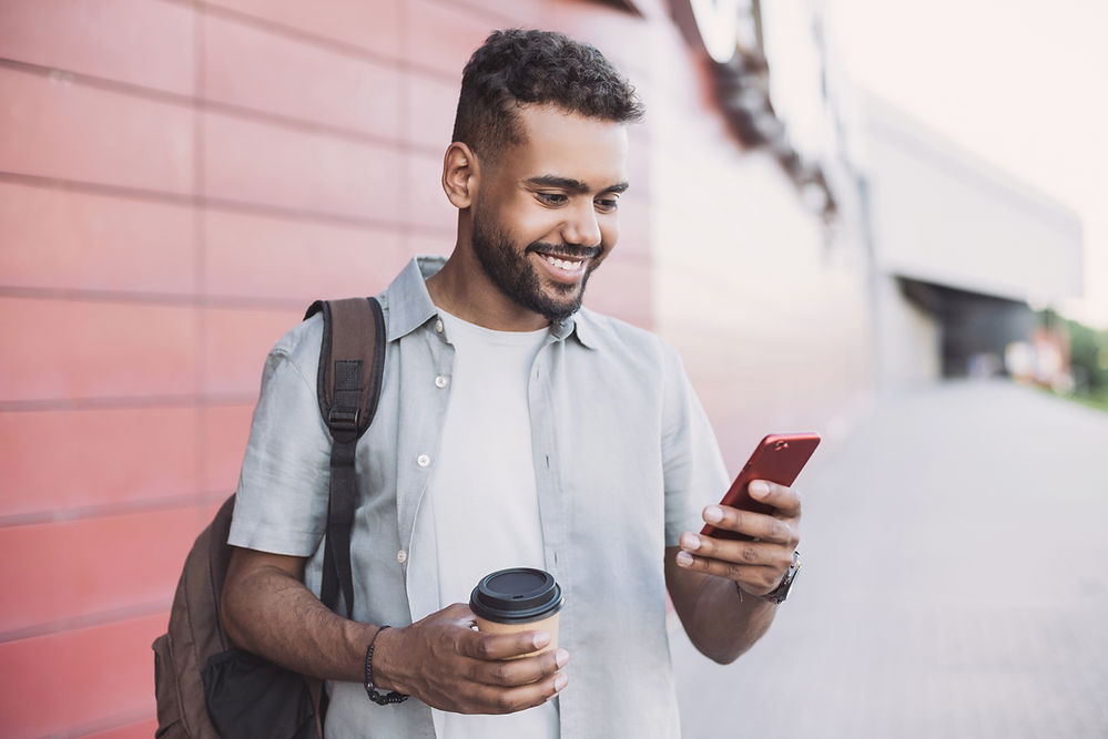 smiling man holding phone and takeaway coffee