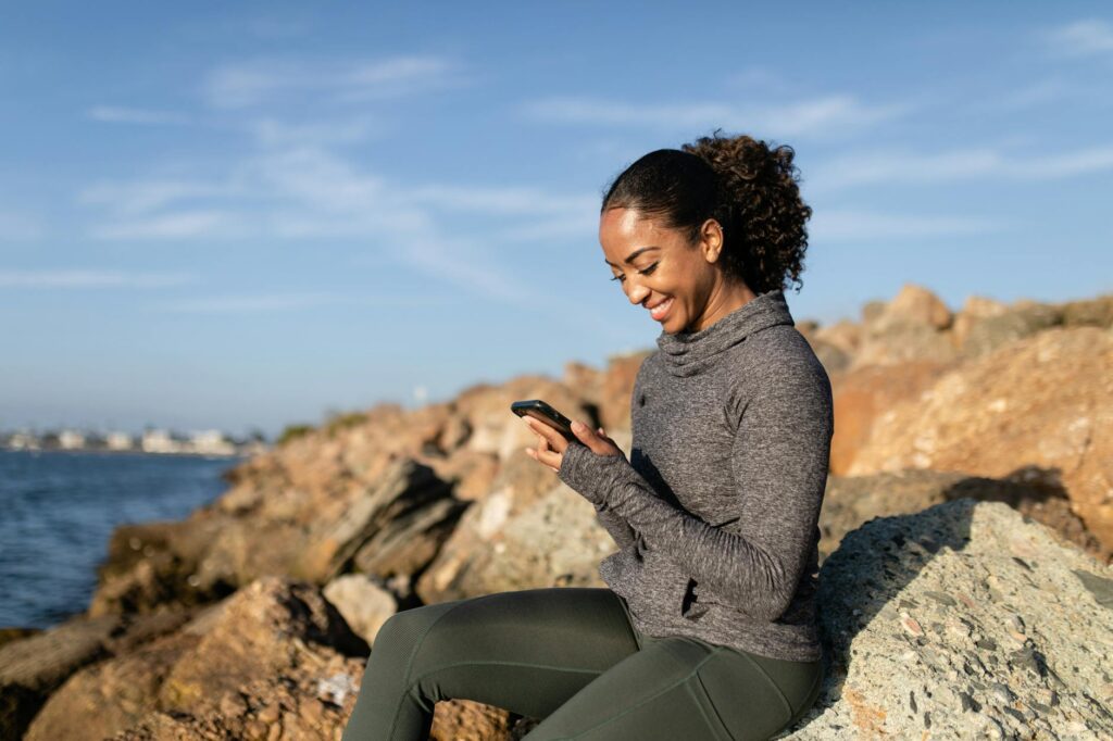 a happy woman using her cellphone while sitting on a rock