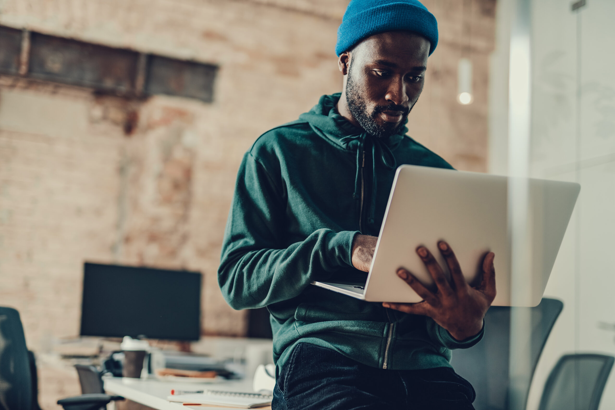 Calm attractive young man in casual clothes sitting alone in the office and using modern laptop while holding it in his hands