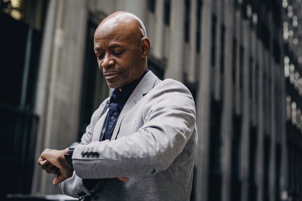 punctual black businessman checking time on wristwatch on street