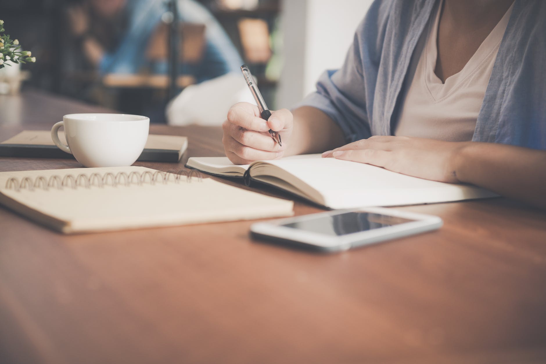 woman writing on a notebook beside teacup and tablet computer for personal loan application with bank